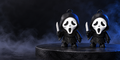 Two black hooded flexible figures with white screaming masks displayed on a dark platform